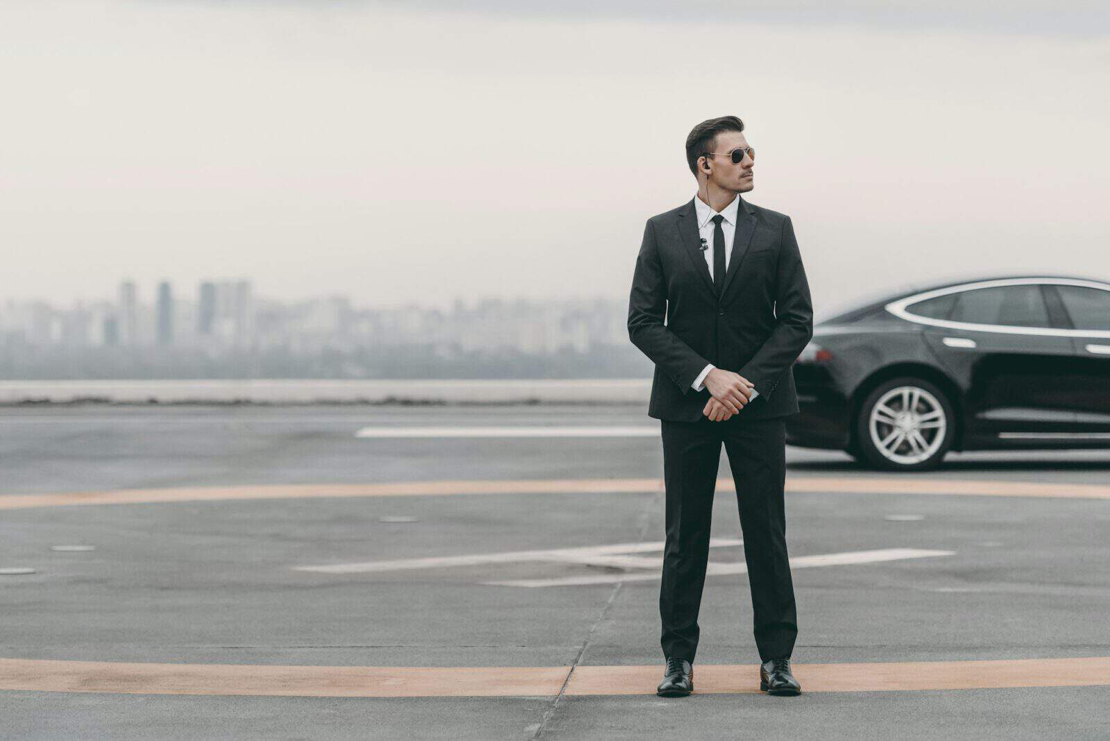 serious bodyguard standing with sunglasses and security earpiece on helipad and looking away